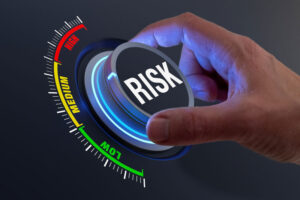 Eine Hand dreht einen Regler auf einer digitalen Anzeige, die das Risikoniveau von "LOW" über "MEDIUM" bis "HIGH" zeigt, mit dem Wort "RISK" prominent auf dem Regler.
