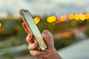Die Hand einer jungen Frau, die ihr iPhone hält und benutzt, vor einem zwielichtigen städtischen Hintergrund.